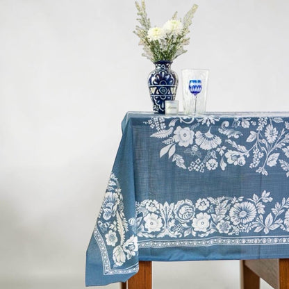 Eclectic soft blue linen-look tablecloth featuring a white floral pattern draped over a wooden table with a vase.