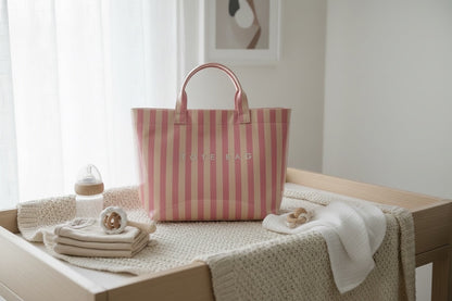 Eclectic blush and neutral stripe PVC carry tote bag on a nursery changing table with baby essentials.
