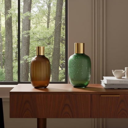 Eclectic brown glass vase with gold rim and vertical texture displayed on a wooden sideboard next to a green vase