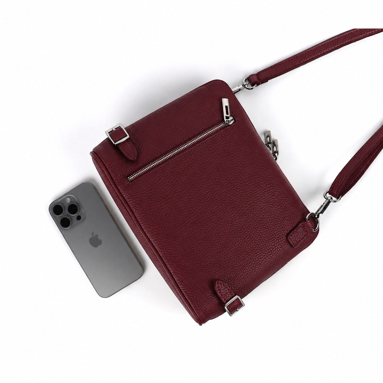 Eclectic Capri burgundy grained leather crossbody bag with silver hardware and rear zip pocket next to a smartphone.