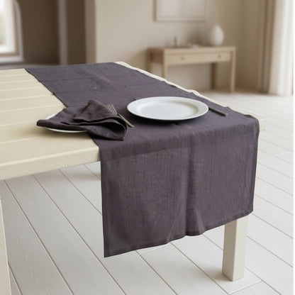 Eclectic charcoal linen table runner with stitched edges on a light wooden table with a matching napkin and plate.