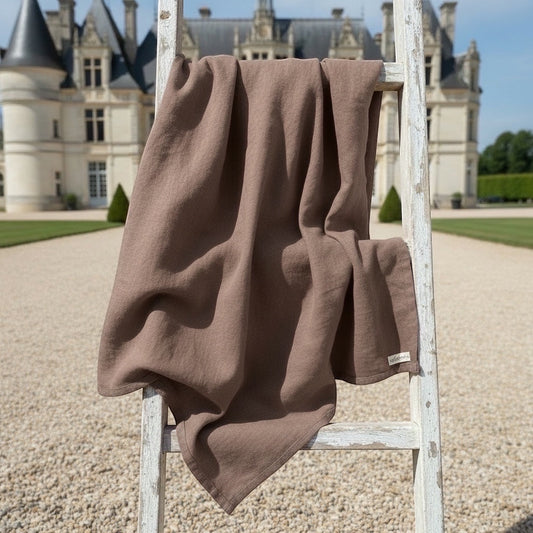 Eclectic Charvet Editions chocolate brown 100% linen tablecloth draped over a rustic white ladder in a French garden.