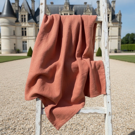 Eclectic Charvet Editions terracotta linen tablecloth draped over a rustic white wooden ladder in front of a chateau.