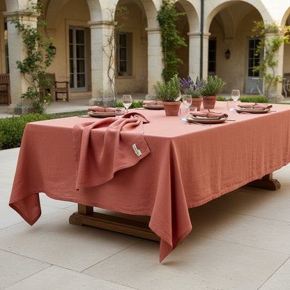 Eclectic Charvet Éditions terracotta linen tablecloth draped over a large outdoor dining table in a stone courtyard.