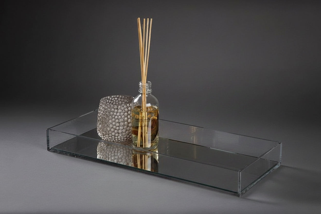 Eclectic clear acrylic mirrored display tray holding a glass reed diffuser and a textured decorative candle holder.