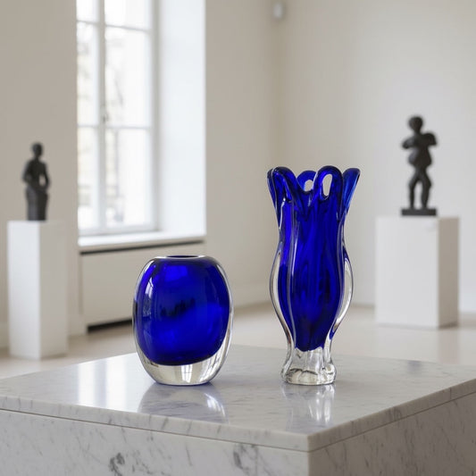 Eclectic cobalt blue art glass vases with rounded and sculptural silhouettes displayed on a white marble pedestal.
