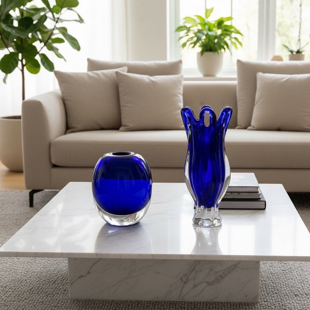 Eclectic cobalt blue art glass vases with sculptural silhouettes displayed on a white marble coffee table.