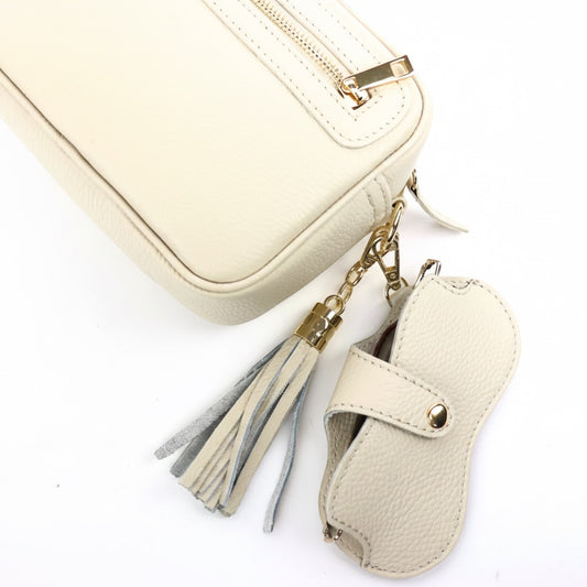 Eclectic cream leather glasses case with gold-tone snap button and clip attached to a matching handbag