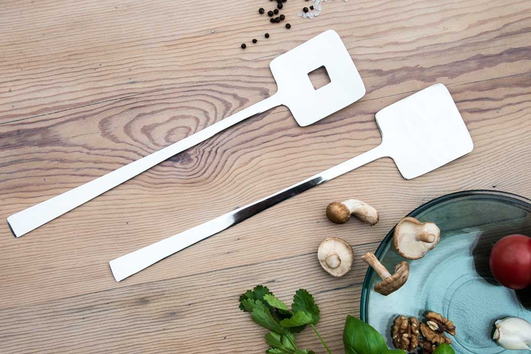 Eclectic Deco geometric stainless steel salad servers with a polished mirror finish on a wooden table