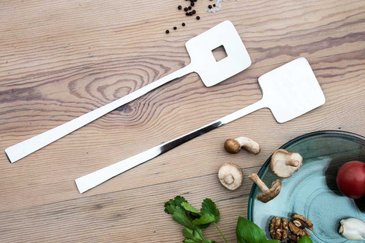 Eclectic Deco geometric stainless steel salad servers with a polished mirror finish on a wooden table