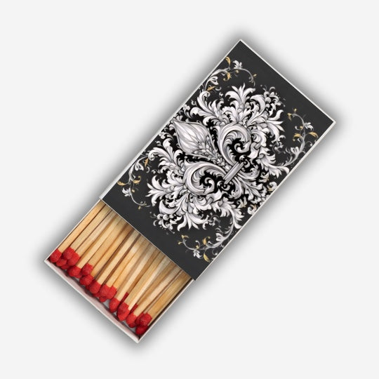 Eclectic decorative matchbox featuring a black and white ornate fleur-de-lis design with long red-tipped wooden matches.
