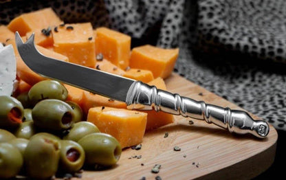 Eclectic Diana Carmichael Ribbon pewter cheese knife with a sculptural vine-inspired handle on a wooden board.