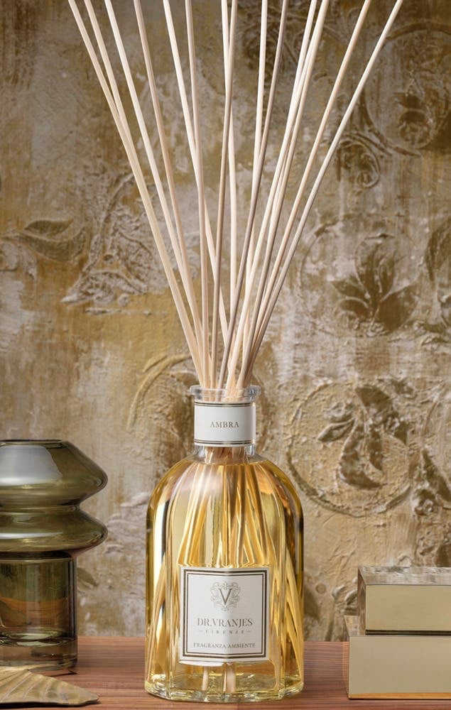 Eclectic Dr Vranjes Ambra reed diffuser in a glass bottle with wooden sticks against a textured gold wall background