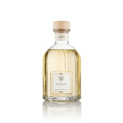 Eclectic Dr Vranjes Ambra reed diffuser in a clear glass bottle with a wooden cap against a black background.