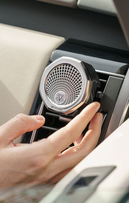 Eclectic Dr Vranjes chrome car air vent diffuser with octagonal design being adjusted by hand in a car interior.