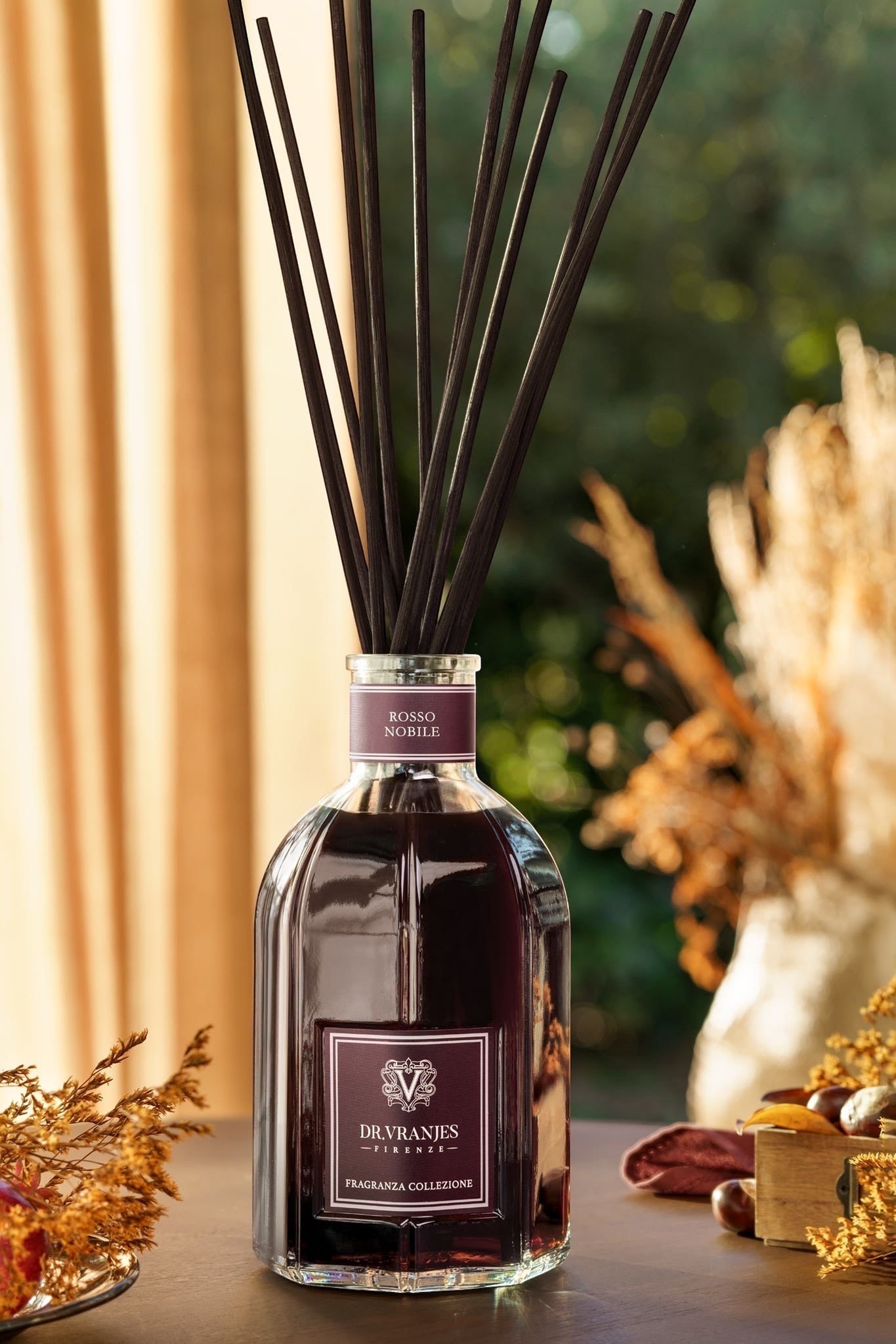 Eclectic Dr Vranjes Rosso Nobile diffuser with dark red liquid and black reeds in a glass bottle on a wooden table