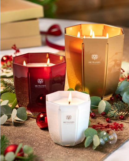 Eclectic Dr. Vranjes scented candles in gold, red, and white hexagonal glass vases with lit wicks on a festive table.