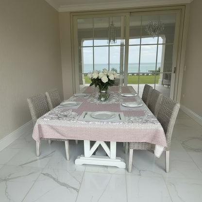Eclectic floral linen-look tablecloth in dusty pink on a dining table with white roses and wicker chairs