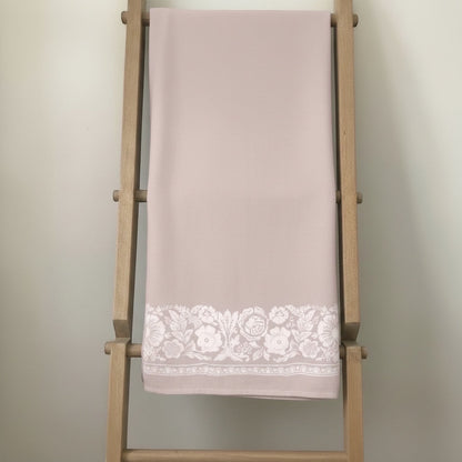 Eclectic dusty pink linen-look tablecloth featuring a delicate white floral border pattern draped on a wooden ladder.