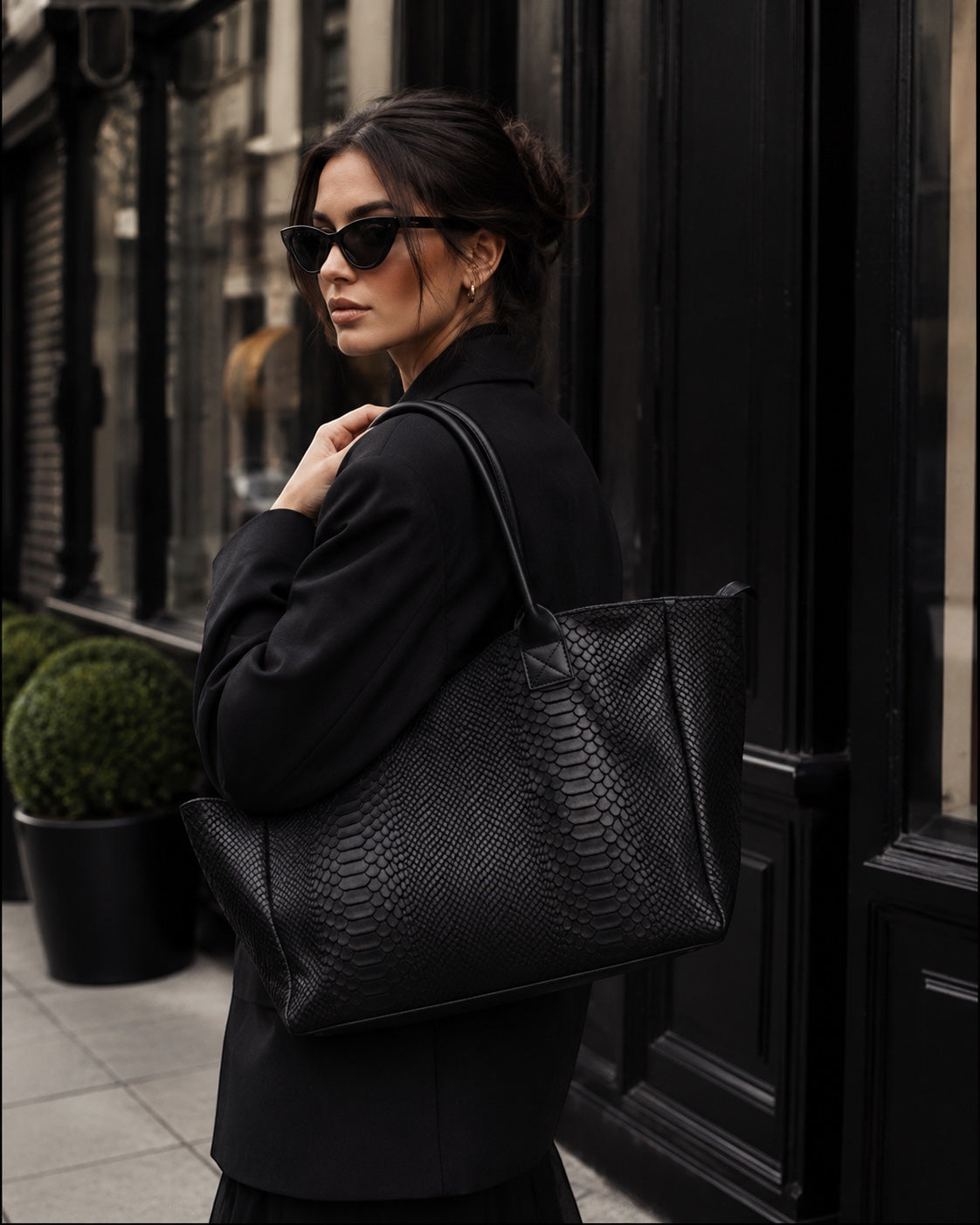 Eclectic Florenza black suede shopper bag with snake-print texture worn over the shoulder by a woman in a black blazer.