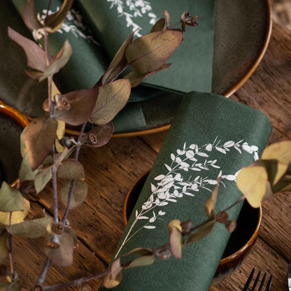Eclectic Françoise Paviot deep green airlaid dinner napkins with white eucalyptus branch print on a wooden table