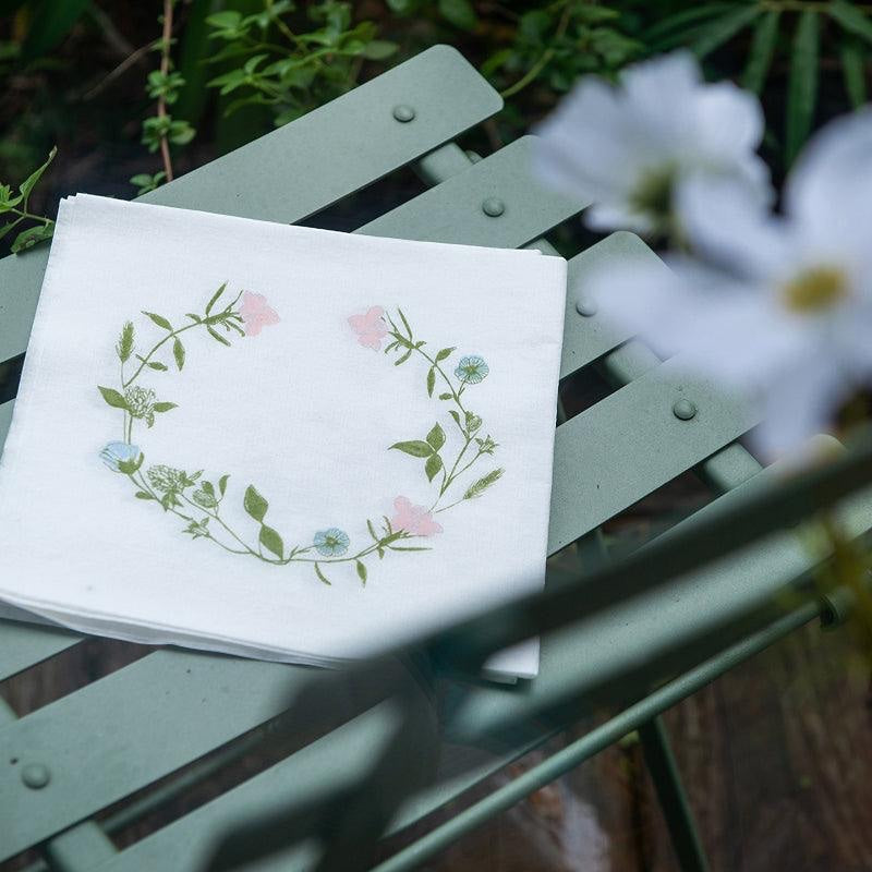Eclectic Françoise Paviot Fleurs des Prés cocktail napkin with a pastel wildflower wreath on a green garden chair
