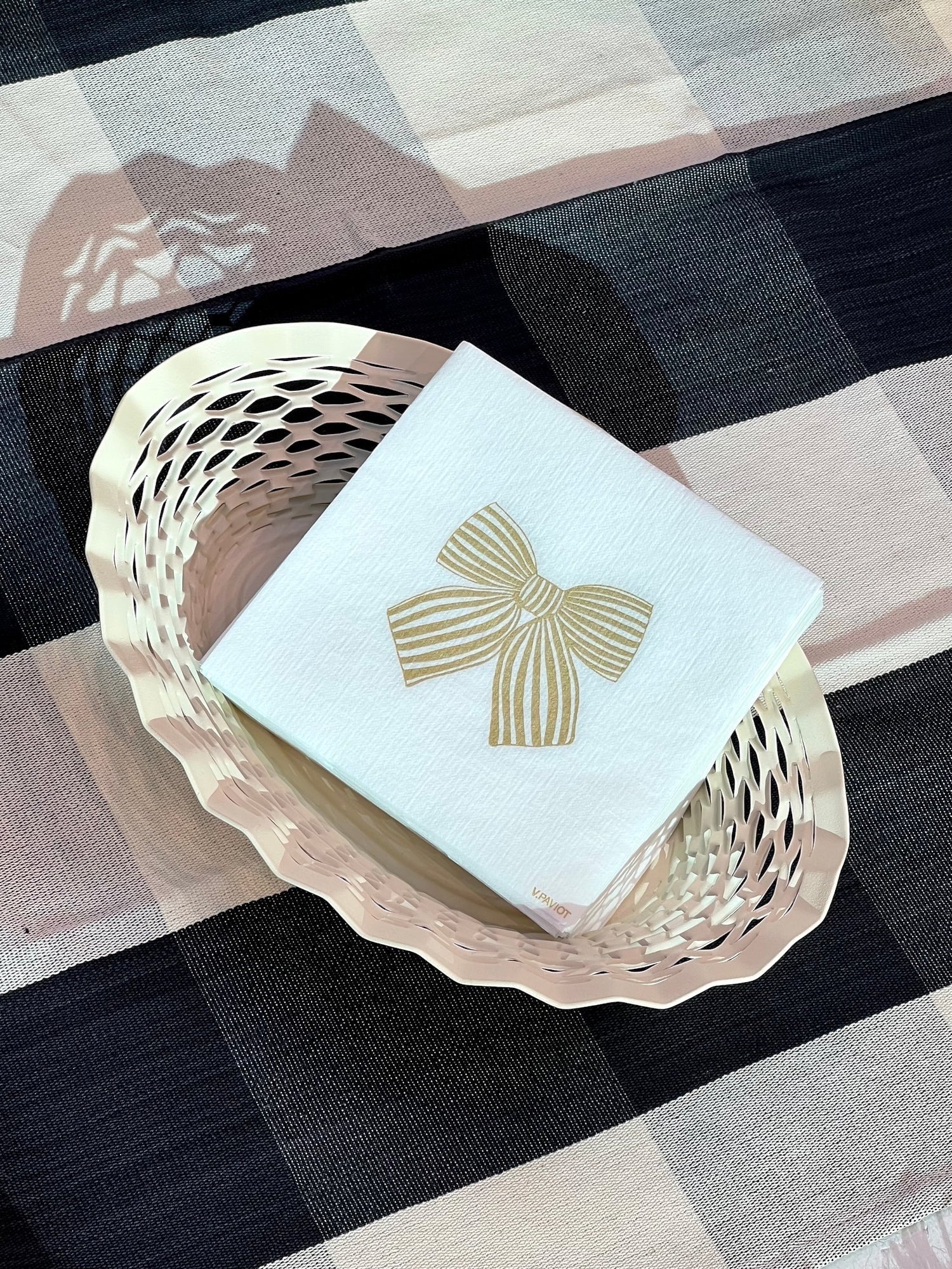Eclectic Françoise Paviot Noeud Or cocktail napkin with a gold bow design in a decorative basket on a plaid cloth.
