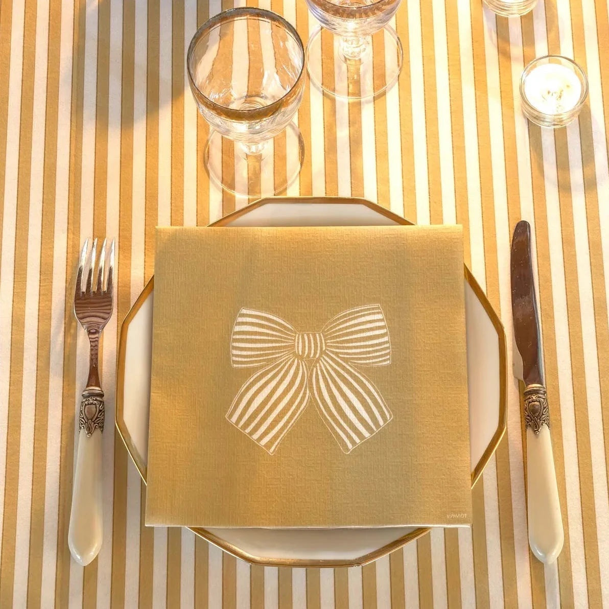 Eclectic Françoise Paviot gold airlaid dinner napkin with white bow design on a place setting with cutlery