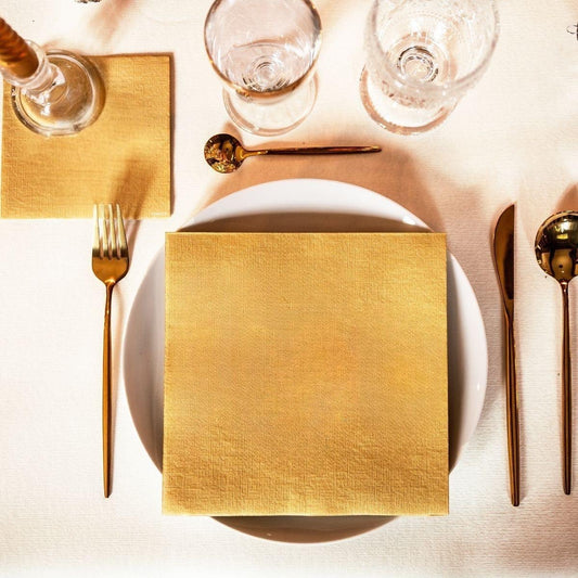 Eclectic Françoise Paviot gold airlaid dinner napkin placed on a white plate with gold cutlery on a table setting