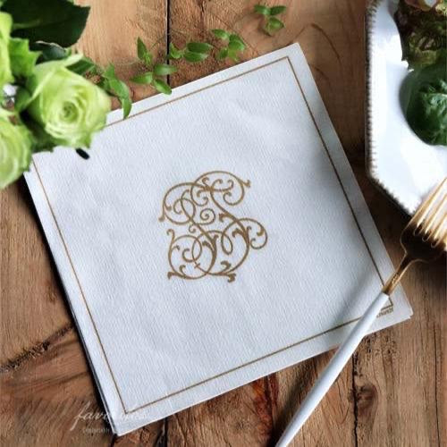 Eclectic Françoise Paviot white airlaid dinner napkin with elegant gold monogram design on a rustic wooden table.