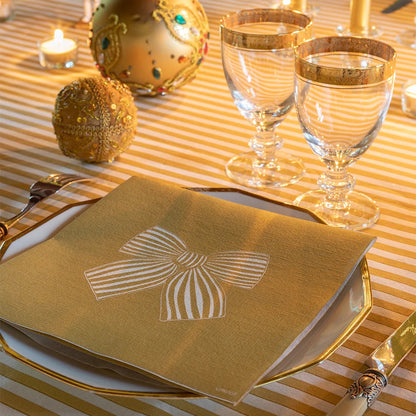 Eclectic Françoise Paviot gold airlaid dinner napkin with white ribbon bow design on a festive table setting