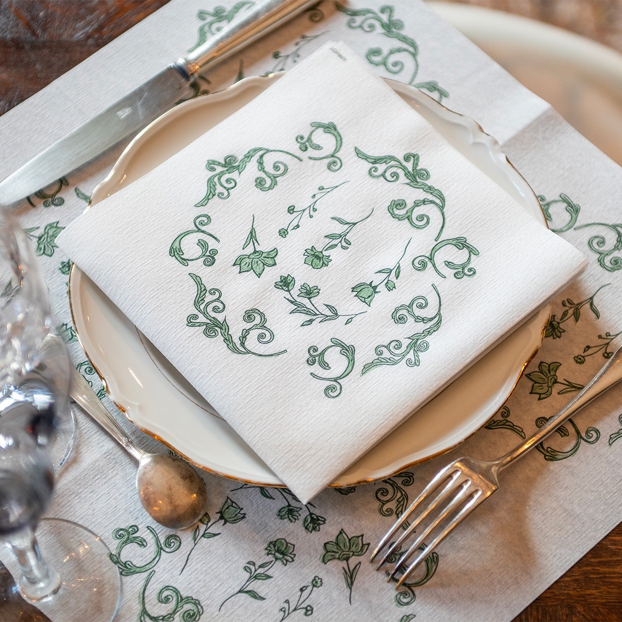 Eclectic Françoise Paviot Régence Vert airlaid dinner napkin with green botanical motifs on a white plate setting.
