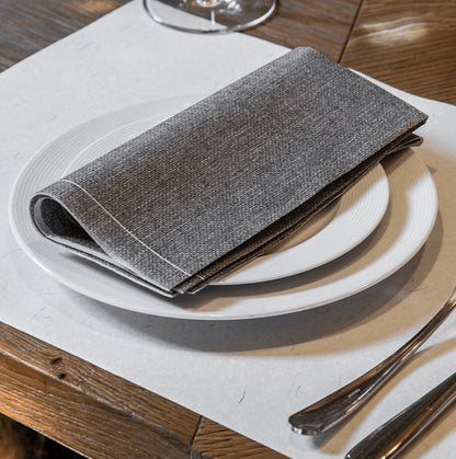 Eclectic Françoise Paviot Chine Gris grey airlaid dinner napkin folded on a white plate on a wooden table