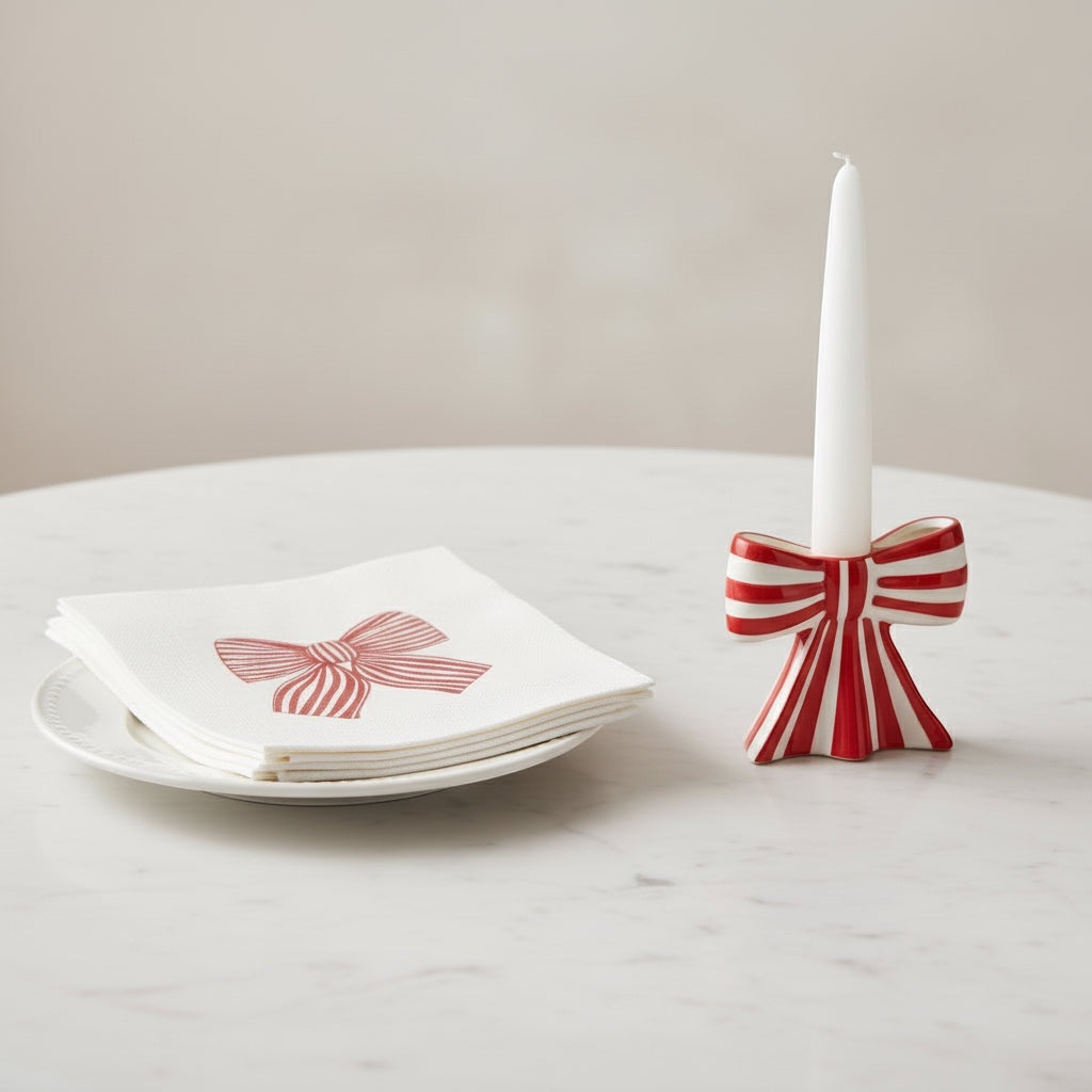 Eclectic Françoise Paviot Noeud Rouge cocktail napkins with red bow print on a plate next to a matching bow candle holder