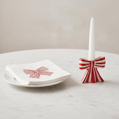 Eclectic Françoise Paviot Noeud Rouge cocktail napkins with red bow print on a plate next to a matching bow candle holder