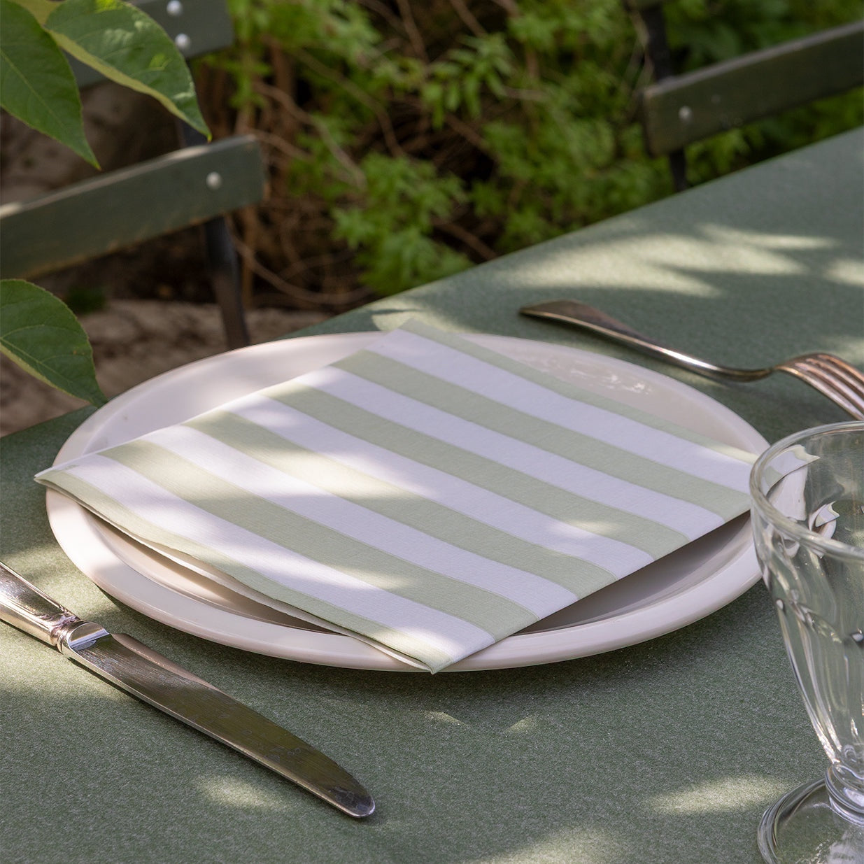 Eclectic Françoise Paviot Rayure Olive striped dinner napkin on a white plate with cutlery on an outdoor table