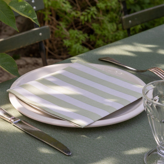 Eclectic Françoise Paviot Rayure Olive striped dinner napkin on a white plate with cutlery on an outdoor table