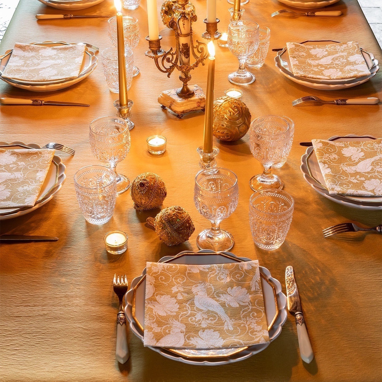 Eclectic Perruche Or dinner napkins by Françoise Paviot featuring gold baroque parrot patterns on a formal table.