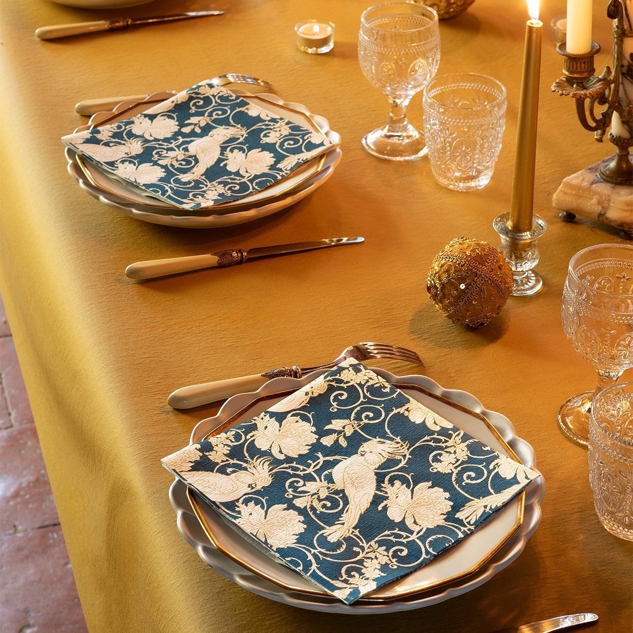 Eclectic Françoise Paviot petrol blue dinner napkins with ivory parakeet and floral motifs on a gold table setting.