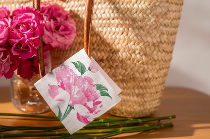Eclectic Françoise Paviot Pivoine cocktail napkin with pink peony floral print hanging from a woven straw bag handle
