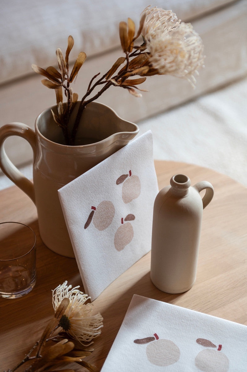 Eclectic Françoise Paviot Pomme airlaid dinner napkins with apple motif on a wooden table with ceramic vases.
