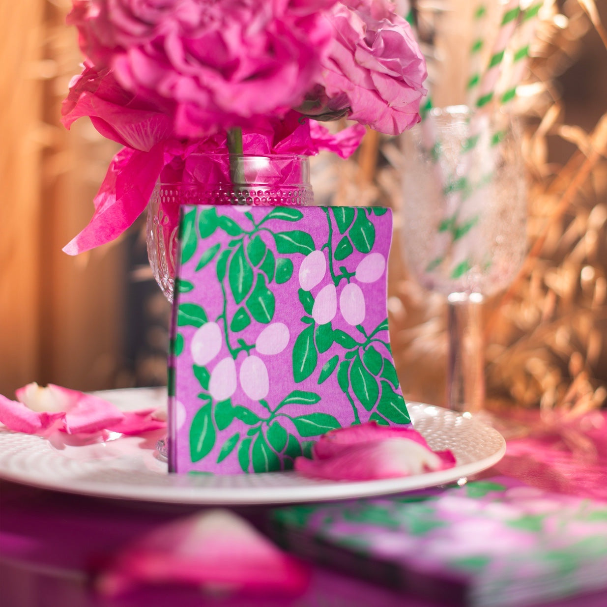 Eclectic Françoise Paviot Prune cocktail napkin with purple plum tree pattern on a decorated table with pink flowers.