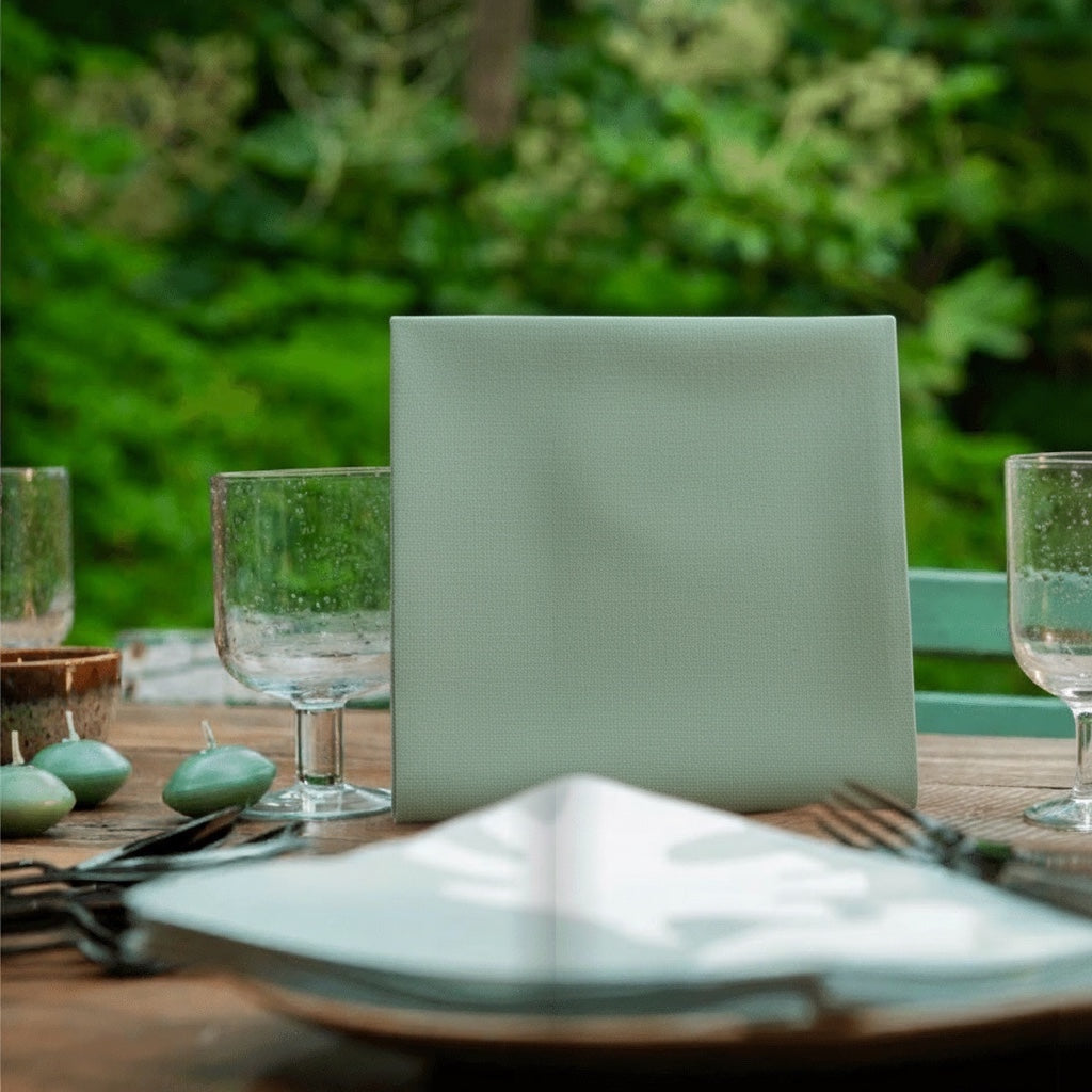 Eclectic Françoise Paviot sage green airlaid dinner napkin standing on a wooden outdoor dining table.