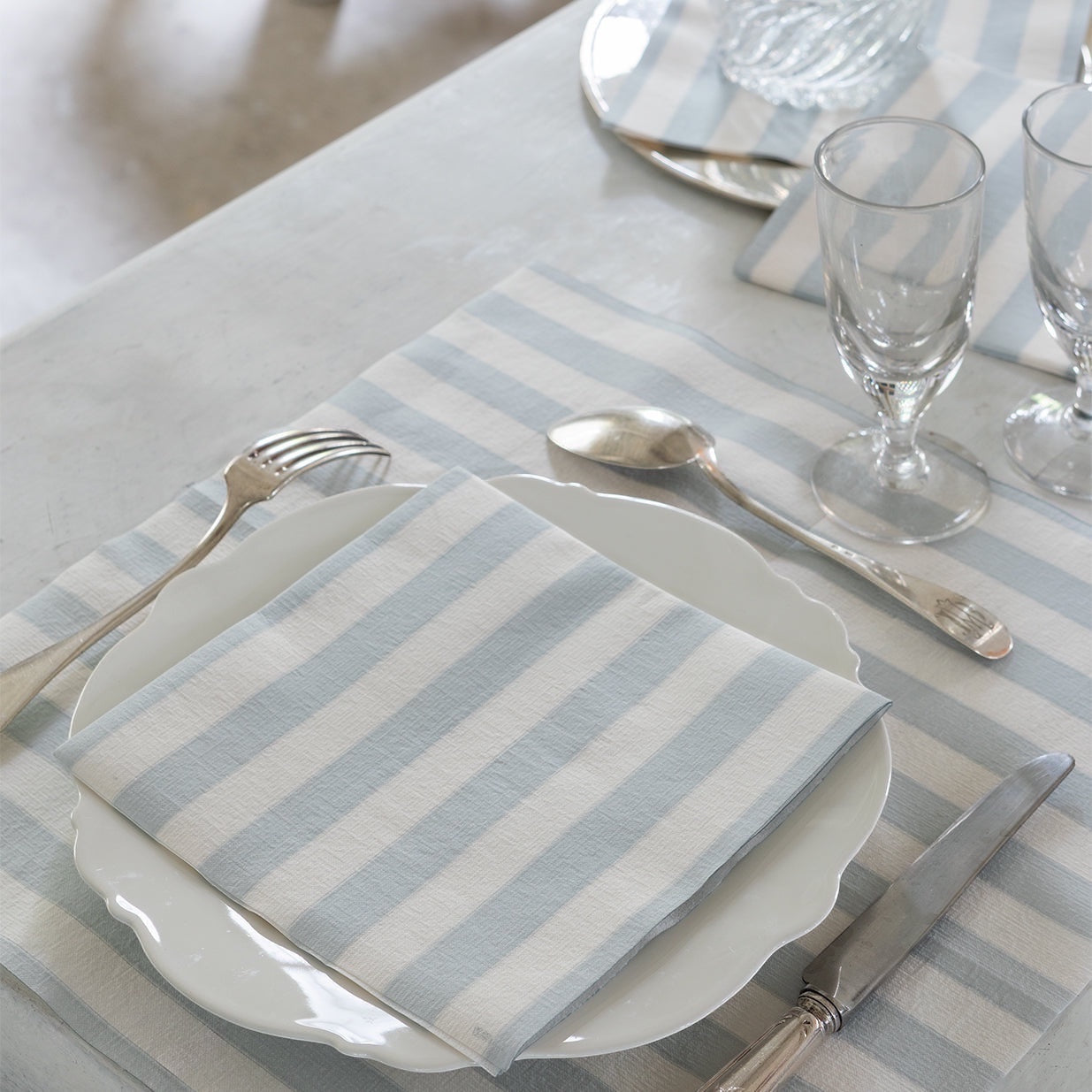 Eclectic Françoise Paviot blue-grey striped airlaid dinner napkin on a white plate with silver cutlery