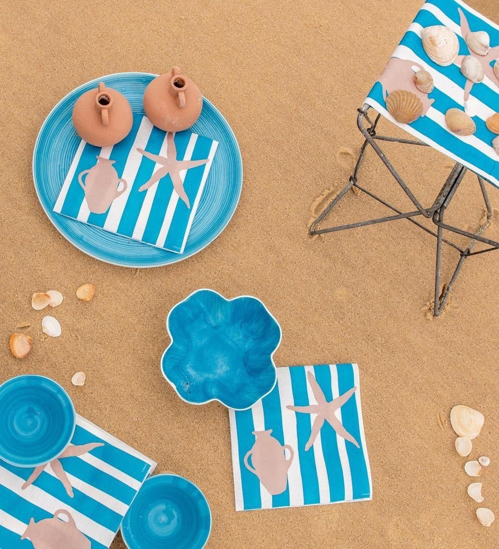 Eclectic Françoise Paviot Transat Bleu airlaid dinner napkins with blue and white stripes on a sandy beach setting.