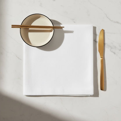 Eclectic Françoise Paviot white airlaid dinner napkin on a marble table with gold cutlery and a small bowl