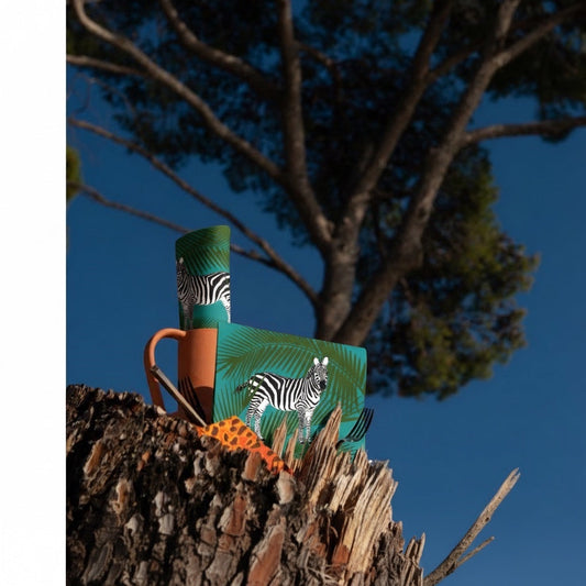 Eclectic Françoise Paviot zebra print cocktail napkins with palm leaf design displayed on a tree stump outdoors.