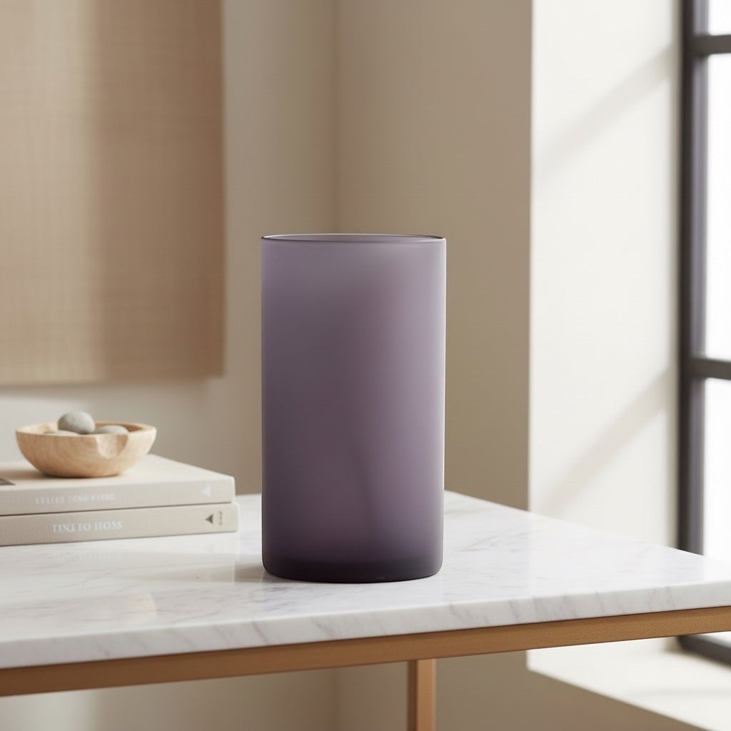 Eclectic frosted plum glass cylinder vase with a matte finish, displayed on a marble table in a modern interior.