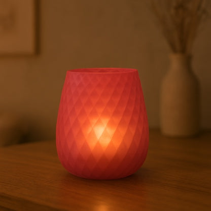 Eclectic frosted strawberry red glass vase and candle holder with a textured diamond pattern glowing on a table