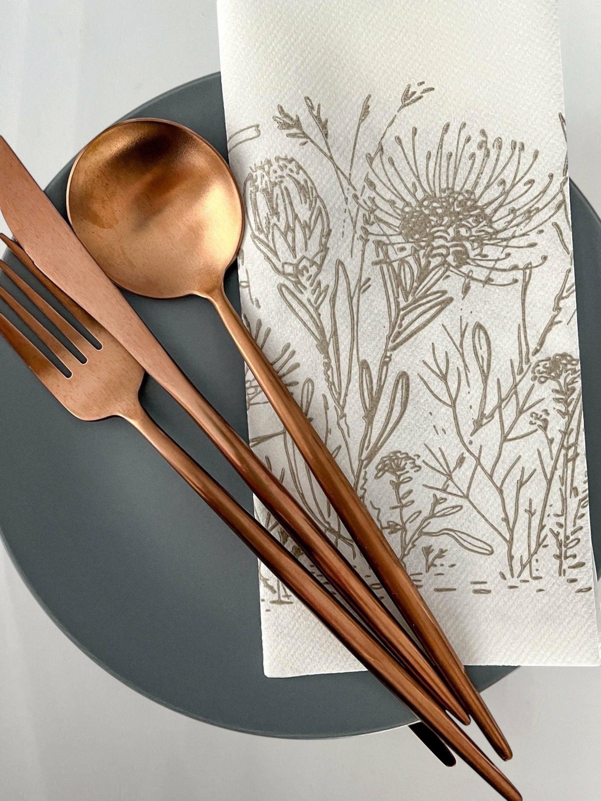 Eclectic Fynbos oatmeal botanical print airlaid napkin on a grey plate with copper cutlery